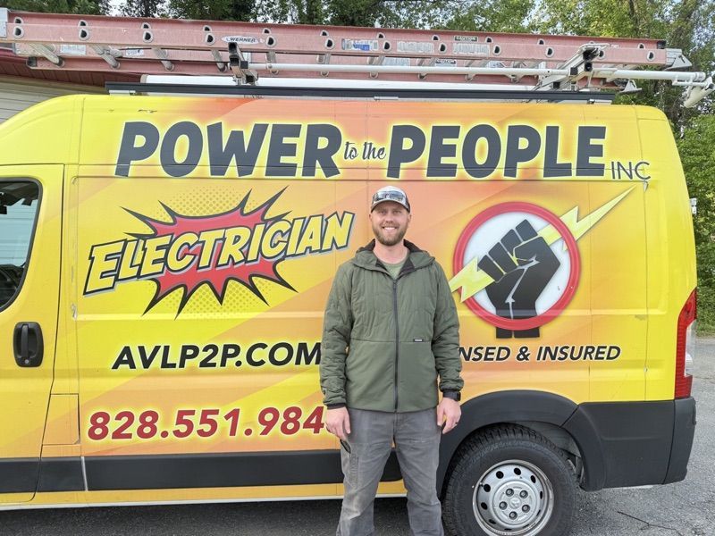 Bearded person in a ball cap and olive jacket, by the yellow company van.