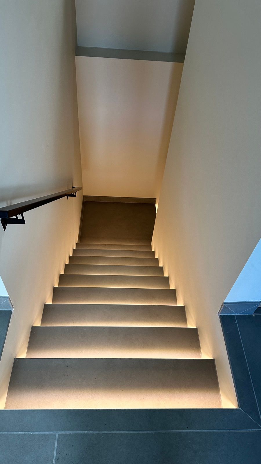 Warm LED step lighting seen from the top of a staircase down to a tiled landing.