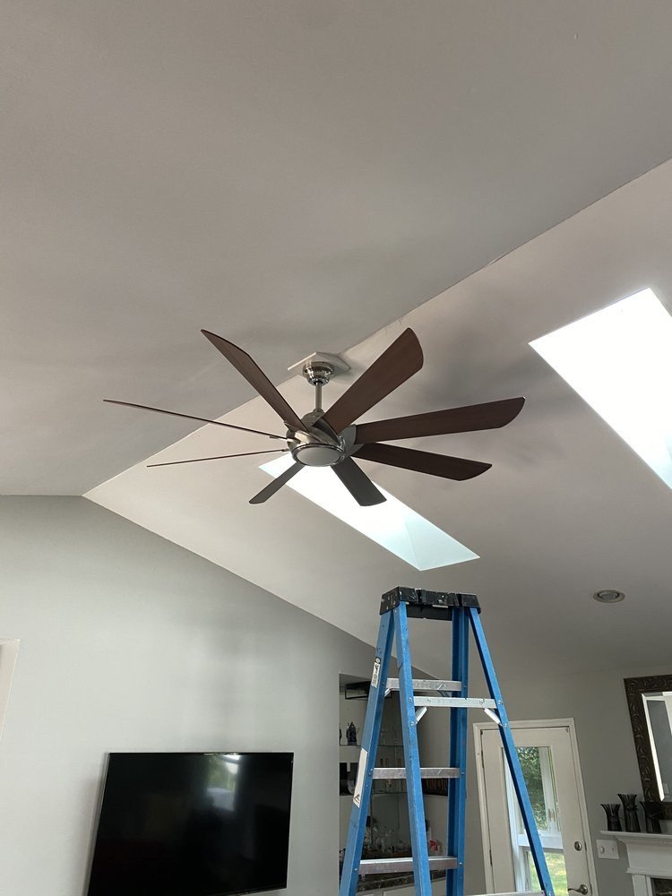 Large eight-blade ceiling fan mounted on a vaulted ceiling beside a skylight in an Asheville great room, with the installer's ladder still in the room
