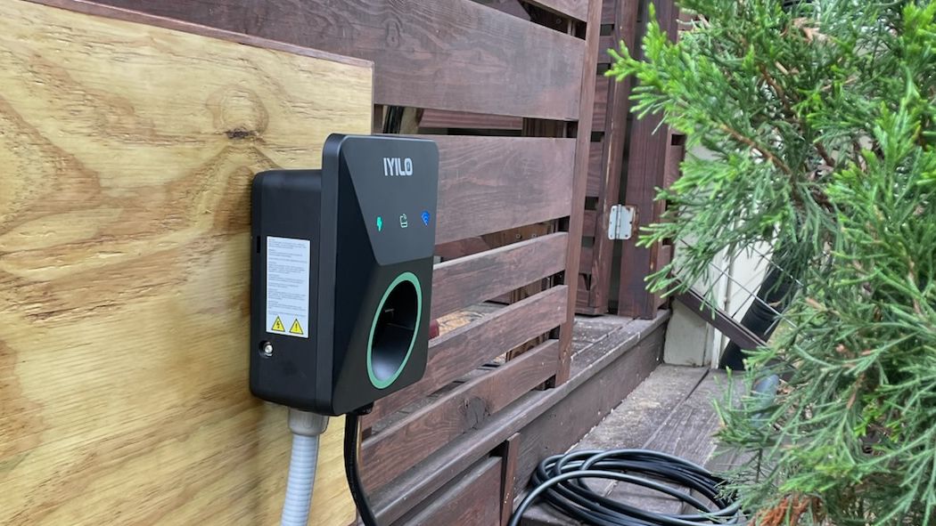 Level 2 EV charger mounted on the exterior wall of an Asheville home, fed by weatherproof flexible conduit, with the charging cable coiled beside it