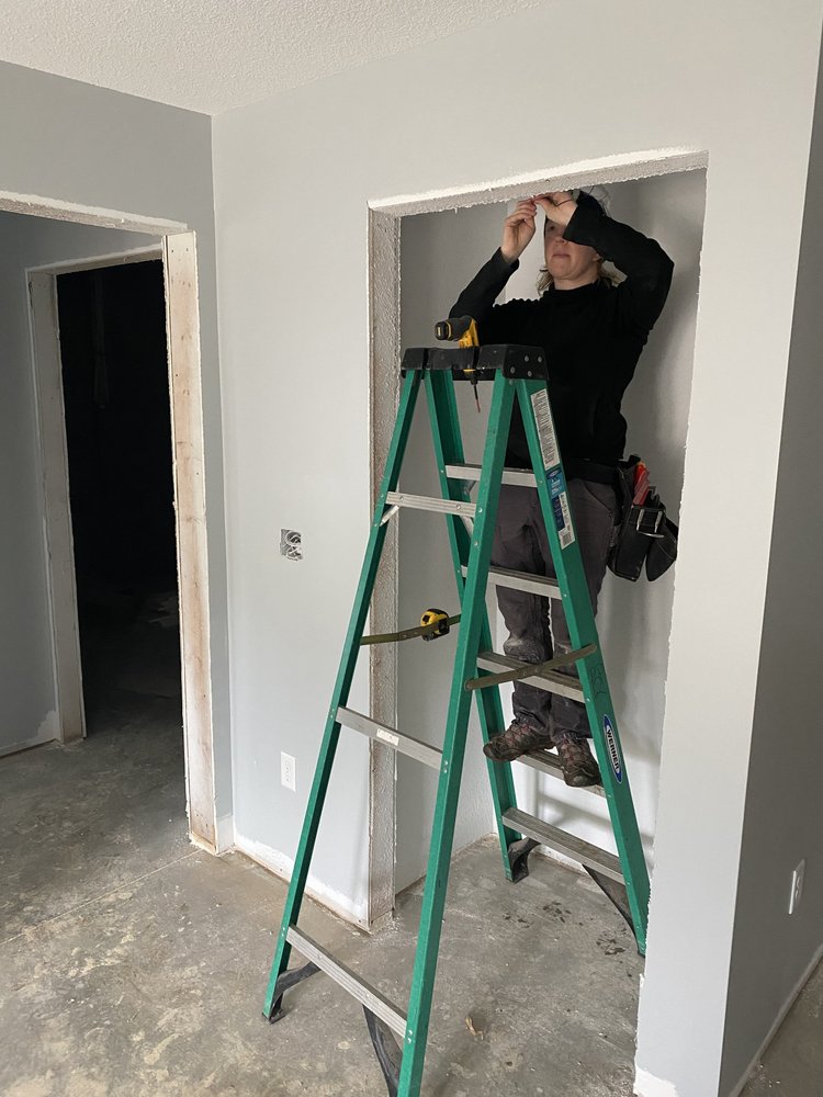 Power to the People electrician working from a green ladder inside a wall opening during a residential Asheville remodel